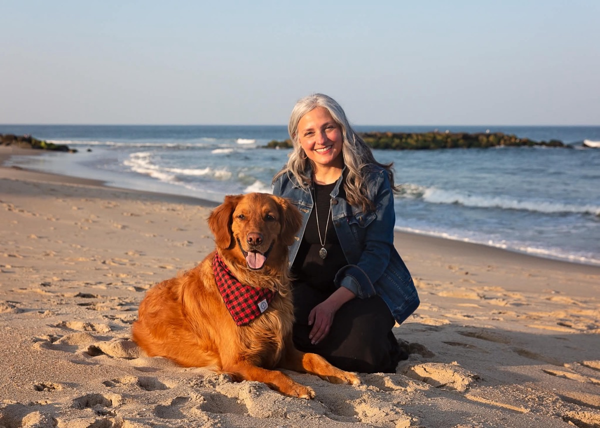 A client sits with her golden retriever on the beach